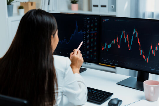 Young beautiful Asian businesswoman pointing with pen in exchange stock market on pc screen at back side view, analyzing profit at modern office, investing high profit valed in wealth. Stratagem.