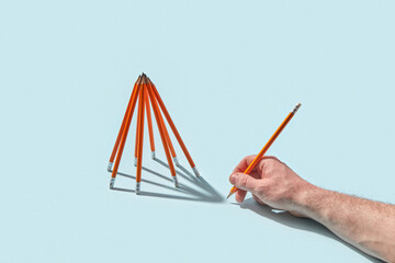 Hand holding pencil near standing pencil structure