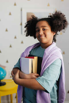 Smart elementary school student girl holding books and digital tablet
