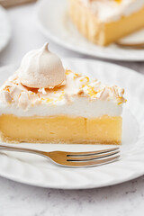 Closeup of a slice of lemon meringue pie on a white plate.