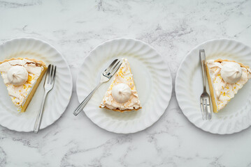Three plates of lemon meringue pie seen from overhead on marble countertop.