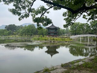 Tranquil view of Gyeonghoeru Pavilion in Gyeongbokgung Palace, Seoul, reflected in a peaceful pond with arched bridge and lush green trees in the background