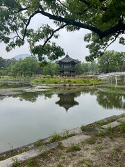 Tranquil view of Gyeonghoeru Pavilion in Gyeongbokgung Palace, Seoul, reflected in a peaceful pond with arched bridge and lush green trees in the background