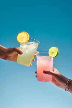 Two refreshing cocktails are raised in a toast against a bright sky