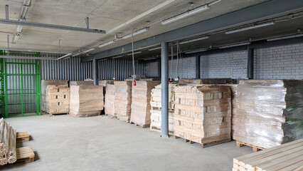 Industrial warehouse stores stacks of wood planks and pallets wrapped in plastic film, ready for storage and transportation