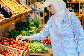 Muslim woman in striped shirt selecting fresh tomatoes at market