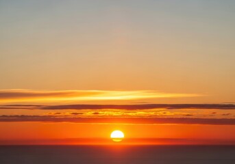 Obraz premium Golden sunset over the calm ocean horizon with vibrant orange and yellow sky and soft clouds