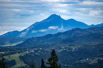 Fototapeta premium Majestic blue mountain range above green forested valley with small village houses