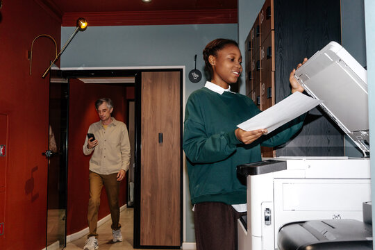 Woman Scanning Documents at Office Printer, Man Checking Smartphone