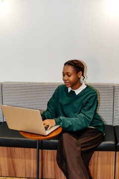 Woman typing on laptop at round table in modern lounge area 