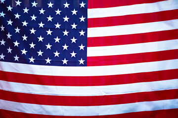 Closeup of a waving American flag mounted on a building with a blue sky in the background