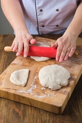 Step by step preparation of steamed bao buns with chicken, fresh cucumber and carrot filling on a wooden background. Rolling out the dough to make buns.