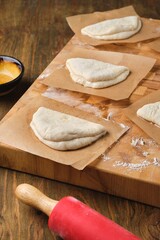 Step by step preparation of steamed bao buns with chicken, fresh cucumber and carrot filling on a wooden background. Rolling out the dough to make buns.