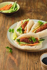 Step by step cooking of steamed bao buns stuffed with chicken, fresh cucumber and carrot on a wooden background. Ready bao buns stuffed with chicken and vegetables on a plate.