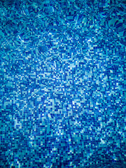 Bright blue mosaic tile texture under rippling pool water with sunlight reflections. Summer aquatic background with clear liquid surface.