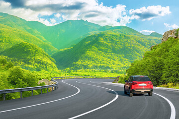 Red car driving on nature road between green mountains in summer. Nature landscape on highway for summer vacation travel. Mountain road view on beautiful nature trip in Europe. car drive on highway.
