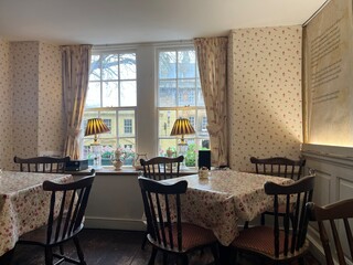 Charming vintage tearoom interior with floral tablecloths, wooden chairs, and cozy window seating overlooking a quaint street view