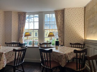 Charming vintage tearoom interior with floral tablecloths, wooden chairs, and cozy window seating overlooking a quaint street view