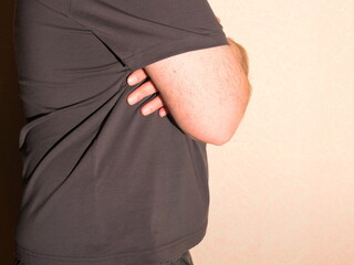 An obese man in a T-shirt shows his belly. Side view