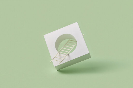 Paper ladder passing through tilted white cube on green