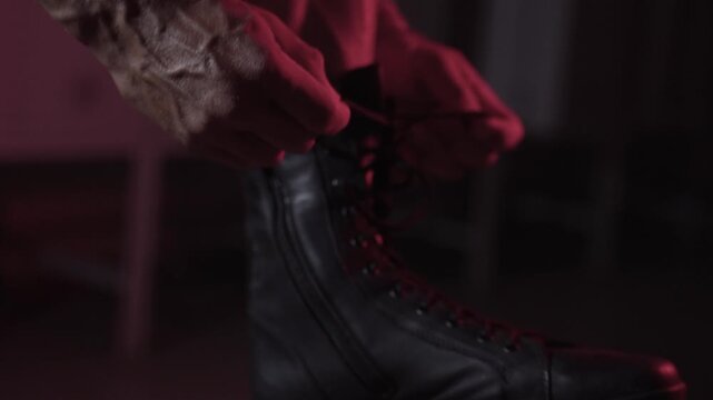Muscular athlete putting on black shoes for training and tying laces close-up in dark room