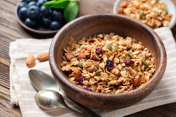 Homemade crunchy oat nut granola with dried cranberries, pumpkin seeds in a wooden bowl