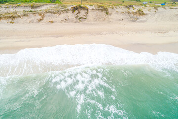 Top view of the shoreline with a turquoise wave and white foam.