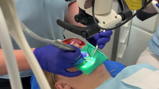 Dentist's hands in gloves with dental punch and cofferdam scarf. Dentist treats woman's tooth to patient with rubber dam. Modern dental office. Treatment elimination of caries, installation of filling