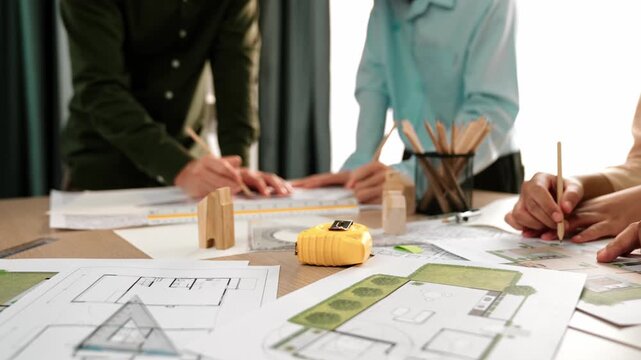 Smart architect and safety engineer discussion about building blueprint on table with architectural document, measurement tools and wooden block scatter around at modern office. Closeup. Delineation.