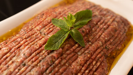 Succulent beef kibbeh nayeh, a Middle Eastern delicacy of finely minced raw beef with bulgur, spices, and olive oil, served with fresh herbs and pita. Traditional Lebanese raw meat dish.