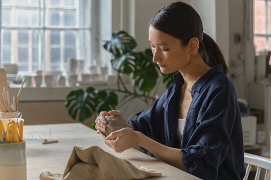 Female Asian ceramics artisan kneads a piece of clay