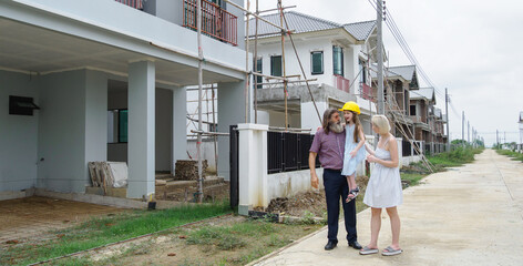 Family consist father mother daughter visit new construction two-story house. pointing at different part building expressing excitement anticipation for their future home. indicat ongoing construction