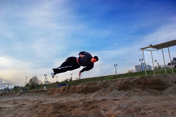 A young guy jumps acrobatic trick on the beach in parkour style against the blue sky	
