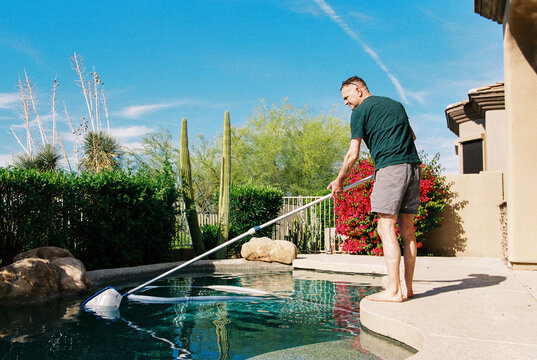 Man cleans backyard swimming pool
