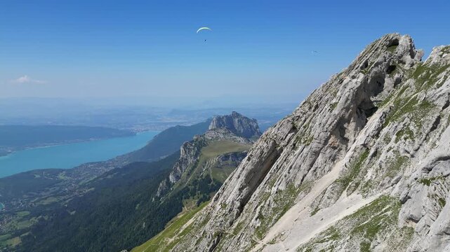 Drone aerial panorama of Lake Annecy and French Alps mountains with paragliders soaring above blue alpine lake, scenic summer travel destination in Haute-Savoie, France
