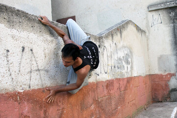 A young guy in a black T-shirt holds on to a vertical wall with his arms and legs	
