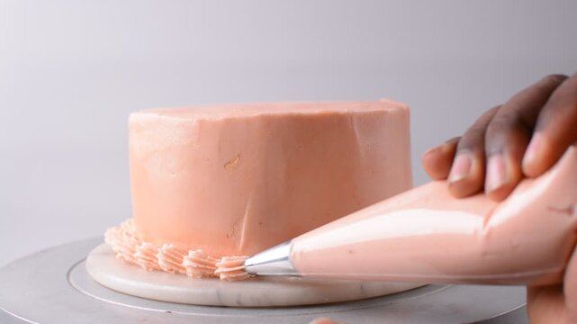 piping border on Pink buttercream cake on a cake plate, Cake covered in pink frosting, process of decorating cake with pink buttercream