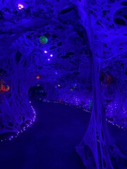Glowing neon Halloween spider decorations with pumpkin faces in a web tunnel under blacklight, creating a spooky and colorful haunted attraction display