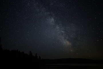 A night scene of a star filled sky and a faint glow of the Milky Way over a calm fresh water lake