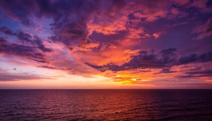 Obraz premium a vibrant sunset sky with dramatic colorful clouds blending orange and blue hues over a distant horizon