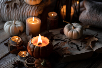 Cozy autumn home still life scene. Ceramic handmade pumpkin mug with burning candle near the window. Fall mood, Thanksgiving concept. Pumpkins, dry leaves, wool sweater, wooden background