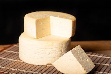 Semi-cured cheese made in Minas Gerais, Brazil, on a rustic surface and dark background, selective focus.