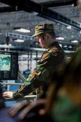Soldier in server hub checking reports at data operations workstation monitor. Army information...
