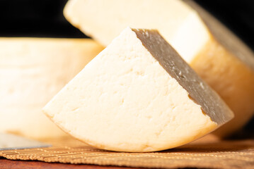 Semi-cured cheese made in Minas Gerais, Brazil, on a rustic surface and dark background, selective focus.