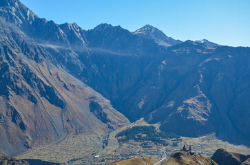 Majestic Caucasus mountain range dominates the background with valley leading to small town...