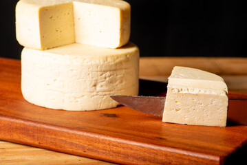 Semi-cured cheese made in Minas Gerais, Brazil, on a rustic surface and dark background, selective focus.