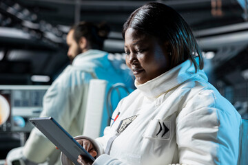 Female astronaut in spacecraft calibrating sensors and conducting safety checks using tablet. Woman in spaceship monitoring life support systems on device during planetary exploration