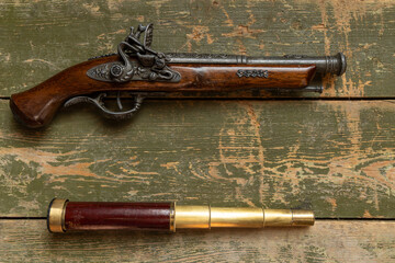 Antique capsule pistol and spyglass on a wooden background.Pirated items on the table. Brass pipe.