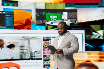 Smiling person uses tablet, streaming online video content during leisure time in modern digital environment. Joyful man browses social media app in front of digital backdrop displaying clips collage