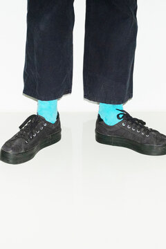 Person with blue socks and pair of black sneakers trainers shoes